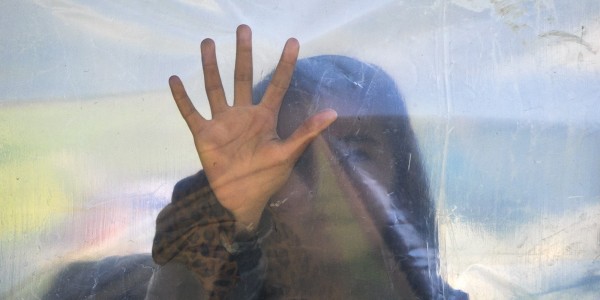 A migrant woman presses her hand against a plastic sheet while waiting for a daily food ration at the northern Greek border point of Idomeni, Greece, Saturday, March 19, 2016. German Chancellor Angela Merkel is urging migrants in the squalid tent city at Idomeni, on the Greek-Macedonian border, to trust Greek authorities and leave for better accommodation as thousands have stayed on site after the closure of Macedonia's border, clinging to hopes the Balkan route used for months by migrants heading for central Europe will reopen.(AP Photo/Vadim Ghirda)